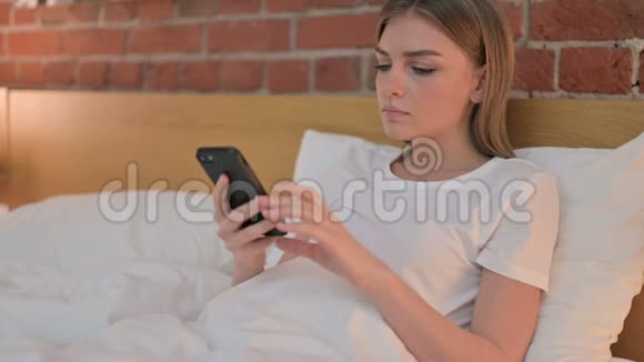 在床上讲智能电话的年轻女性视频的预览图