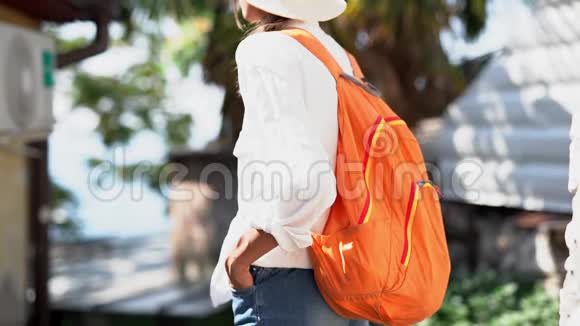 棕榈岛上戴草帽白衬衫和橙色背包观光的快乐女游客视频的预览图