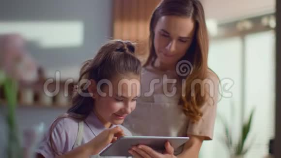 母亲和女儿在厨房里用平板电脑女人在家里和女孩说话视频的预览图