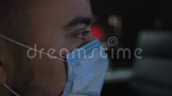 戴着医用面具的男性在家中观看有关冠状病毒的突发新闻视频的预览图