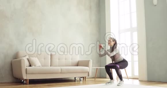 运动女孩训练使蹲在家里在客厅侧视视频的预览图