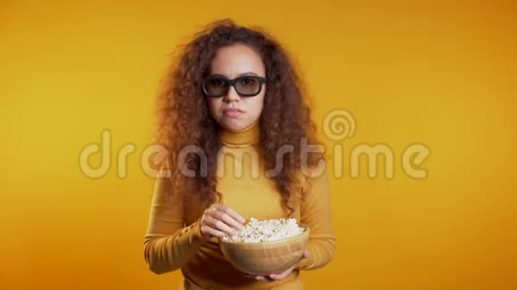 年轻女子在3d眼镜看电影和吃爆米花的黄色工作室背景视频的预览图