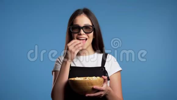 年轻的亚洲女孩戴着3D眼镜看着迷人的喜剧电影笑着吃蓝色爆米花视频的预览图