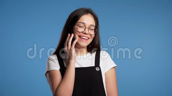 一个留着长发的亚洲女孩在电话里讲话从对话者笑话中不礼貌地笑视频的预览图