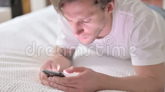 野心勃勃的年轻人在床上玩智能手机视频的预览图