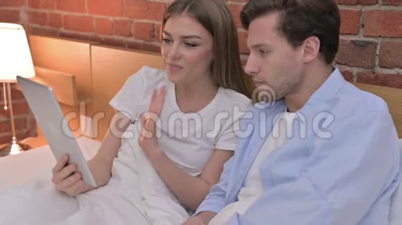 年轻夫妇在床上的平板上进行视频聊天视频的预览图