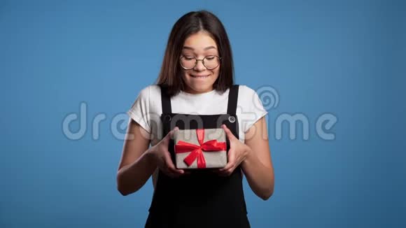 兴奋的亚洲女孩收到了带有蝴蝶结的礼品盒她因受到关注而感到高兴和受宠若惊蓝色女孩视频的预览图