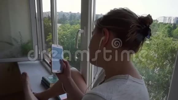 戴着耳机的女孩把头靠在阳台上的窗户上窗台视频的预览图