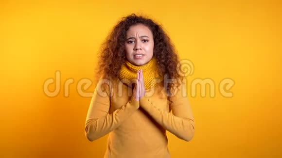 可爱的卷发少女在黄色背景下祈祷女人求人4k视频的预览图
