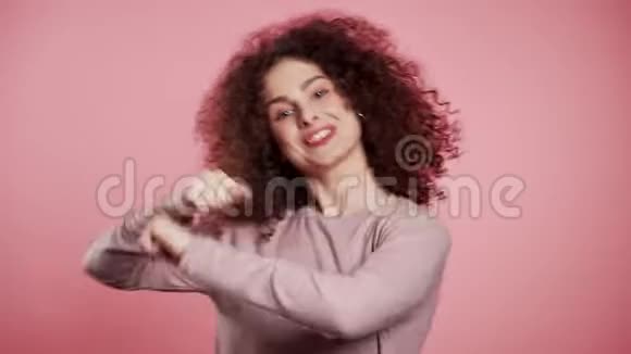 美丽的女人卷曲的头发头在粉红色的工作室背景上跳舞视频的预览图