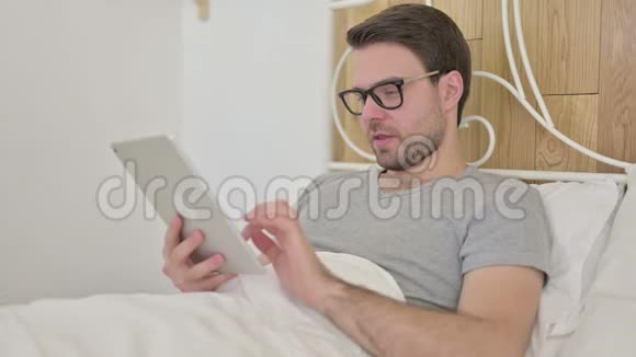 胡子青年男子在床上的平板上得到惊喜视频的预览图