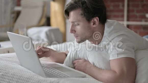 野心勃勃的年轻人在床上用电脑聊天视频的预览图