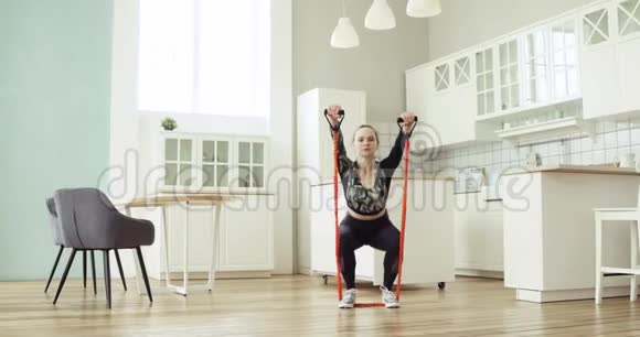 女性使用运动扩张器蹲在厨房的健身训练在家里视频的预览图