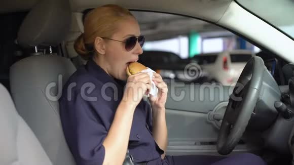 饥饿的女警察坐在停车场的警车里吃汉堡垃圾食品视频的预览图