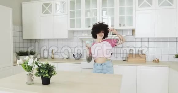 幸福的卷发少女正在厨房里跳舞喝咖啡视频的预览图