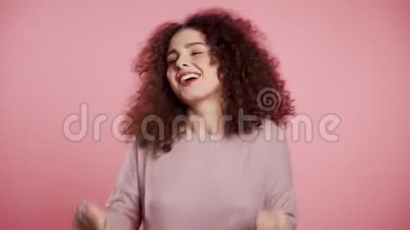 美丽的女人卷曲的头发头在粉红色的工作室背景上跳舞视频的预览图