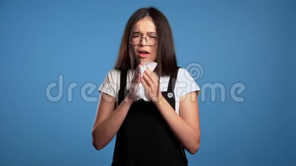 年轻的亚洲女孩打喷嚏成纸巾在蓝影院背景下的孤独女人生病了视频的预览图