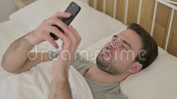 小胡子在床上摆弄智能手机视频的预览图