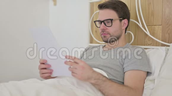 大胡子青年在床上阅读文件视频的预览图