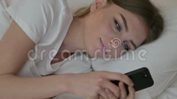 床上使用智能手机的有魅力年轻女性画像视频的预览图