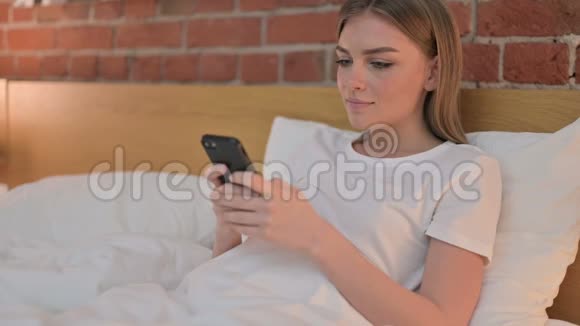 在床上使用智能手机的年轻女性视频的预览图
