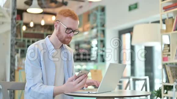 红发男子在咖啡厅使用智能手机和笔记本电脑视频的预览图