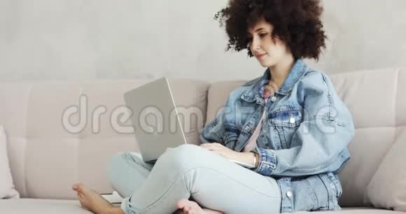 坐在沙发上的笔记本电脑上有卷发的女人在社交媒体上留言视频的预览图