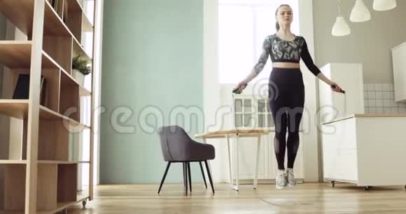 年轻的运动女子正在厨房的家里跳绳做有氧训练视频的预览图