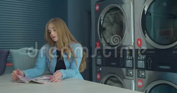 年轻女子在洗衣店洗衣服时看杂志视频的预览图