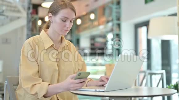 在咖啡厅使用智能手机和笔记本电脑的年轻女子视频的预览图