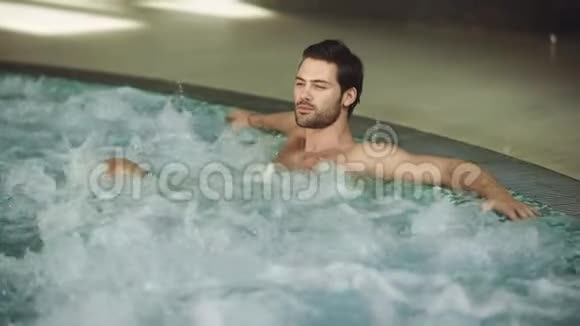 迷人的男人休息按摩浴缸室内快乐的人在游泳池里放松视频的预览图