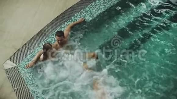幸福的家庭在室内游泳池水疗中心休息年轻夫妇享受按摩浴缸视频的预览图