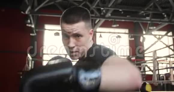 拳击手戴手套拳击和在健身房看相机的年轻人的肖像视频的预览图