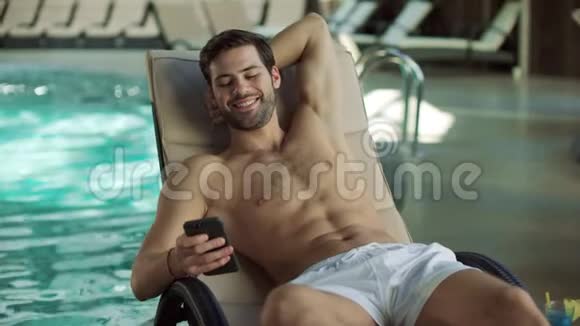 在泳池边用手机做特写快乐男人放松电话视频的预览图