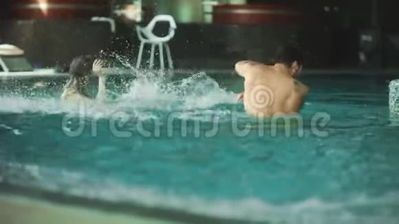 微笑的夫妇在酒店的游泳池里飞溅快乐的夫妻在水中嬉戏视频的预览图