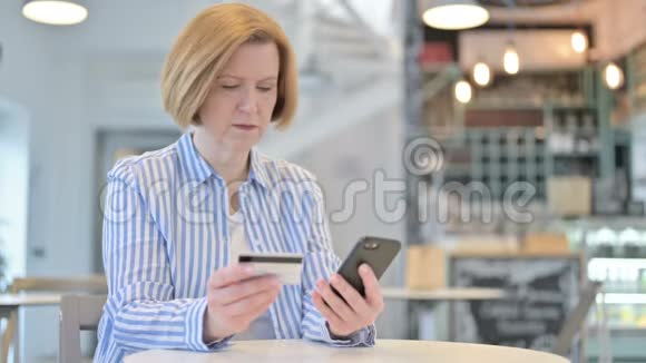 创意老女人在咖啡厅在线支付智能手机视频的预览图