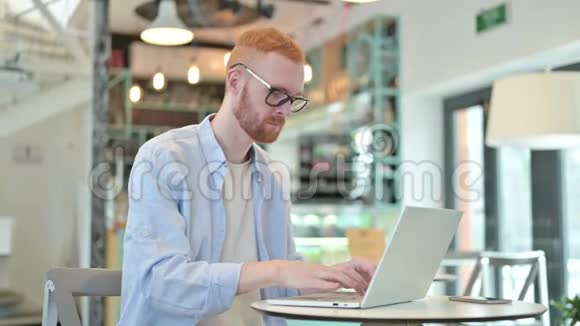 红发男子背部疼痛使用笔记本电脑在咖啡厅视频的预览图