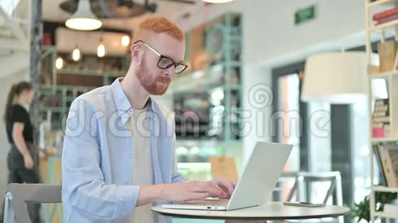 红发男子手提电脑在咖啡厅镜头微笑视频的预览图