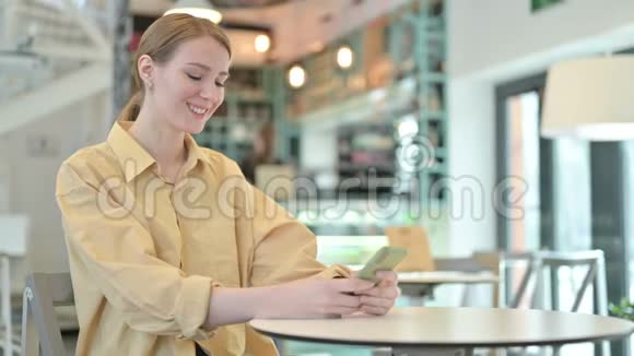 在咖啡厅使用智能手机的微笑青年女子视频的预览图