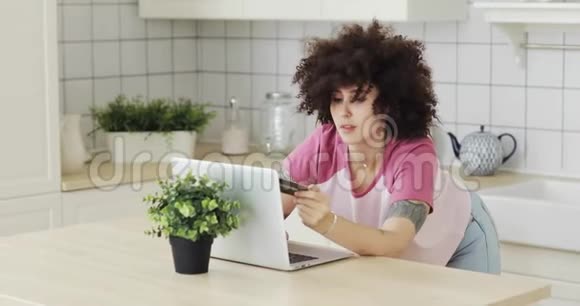 年轻女孩在家里用现代笔记本电脑在线支付银行卡视频的预览图