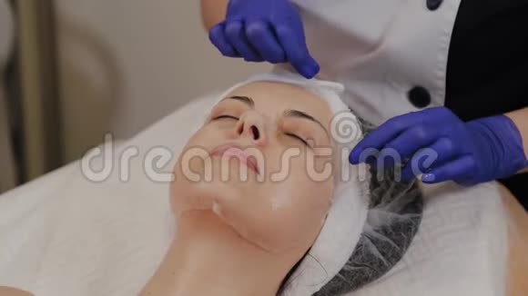 专业美容师从女人的脸上取出透明织物抗衰老面膜视频的预览图