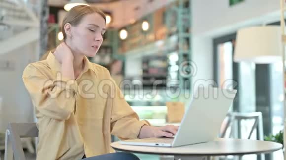颈部疼痛的年轻女子在咖啡厅使用笔记本电脑视频的预览图