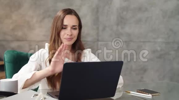 在现代办公室里商务女性在笔记本电脑摄像头上打网络电话视频的预览图