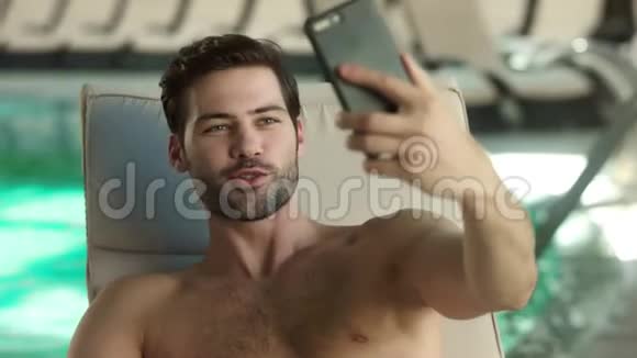 在游泳池附近为现场视频摆姿势的性感男人的肖像拍自拍的搞笑家伙视频的预览图