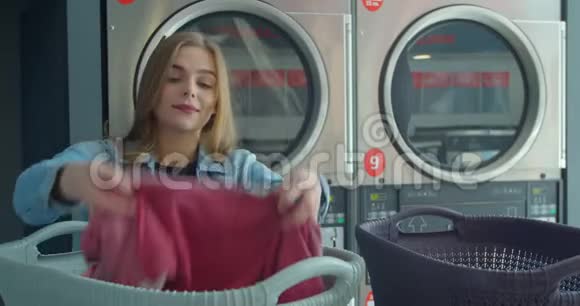 年轻女子整理衣服站在自助洗衣店洗衣服视频的预览图