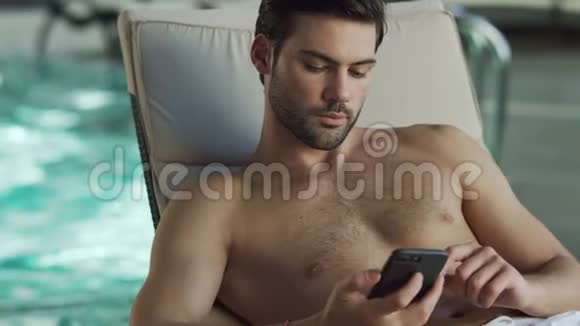 特写男在泳池边看电话男性在健康中心用电话放松视频的预览图