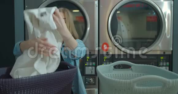 年轻女子整理衣服站在自助洗衣店洗衣服视频的预览图