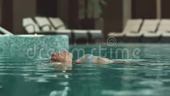 在酒店后面游泳的贴身女人在豪华酒店的游泳池里漂浮的女人视频的预览图