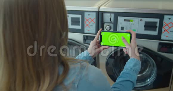 女士在洗衣店洗衣服时使用带有绿色屏幕的智能手机铬钥匙快关门视频的预览图