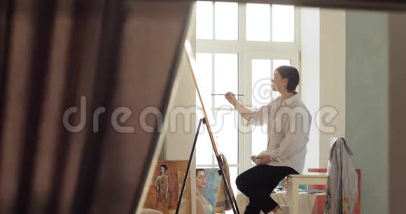 画家正在画架上画一幅画坐在靠近窗户的地方视频的预览图